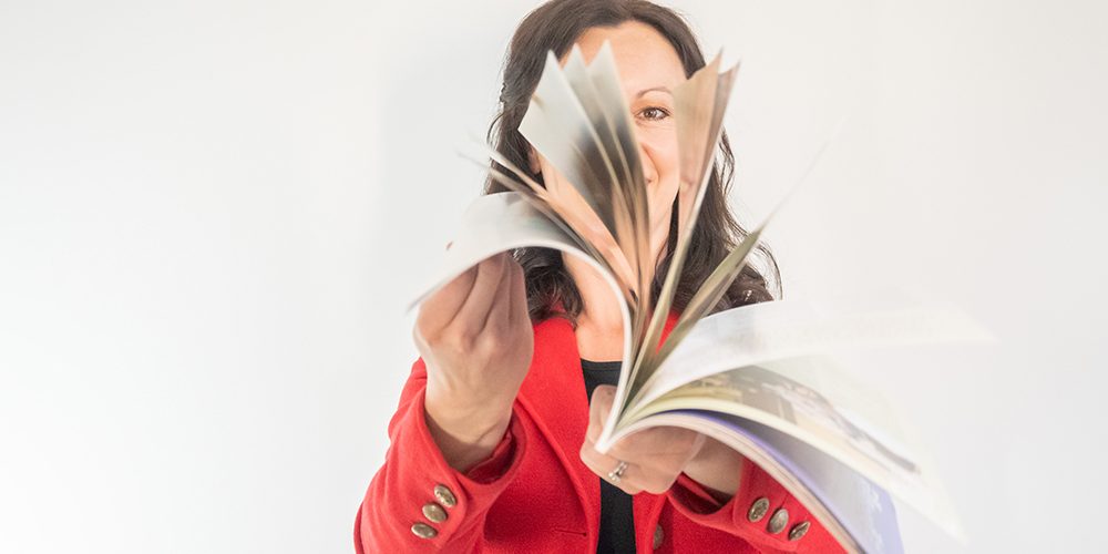 Yvonne is shown flipping pages of a magazine while she peeps through the pages.