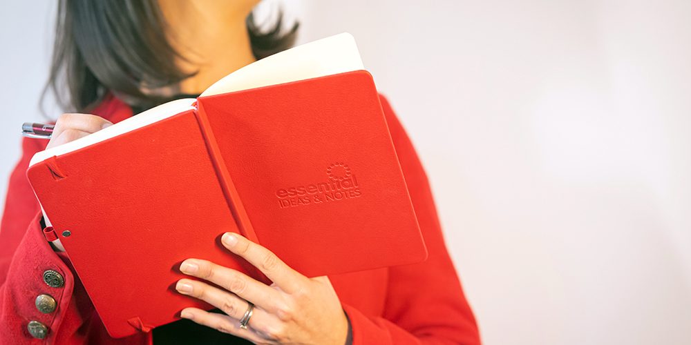 Essential-Print-Services-Notebooks Yvonne is shown holding a branded red notebook with the words Essential Ideas on the front