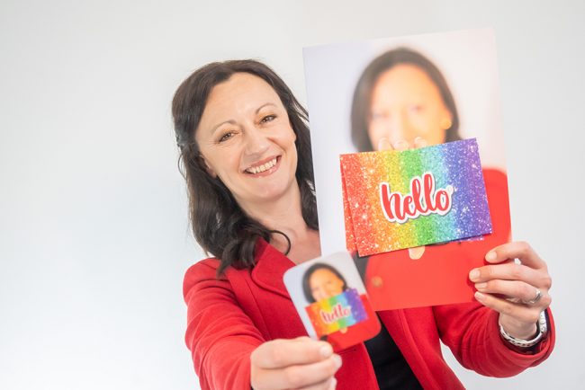 Yvonne Gorman at Derby Essential Print Services Free Artwork Check Yvonne is shown holding her business card and a brochure with the word 'Hello' on the front. Yvonne is smiling.