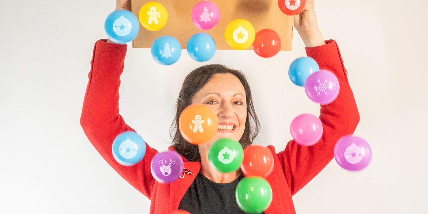 Yvonne is holding a box, tipping out lots of colourful baubles. Yvonne is smiling.