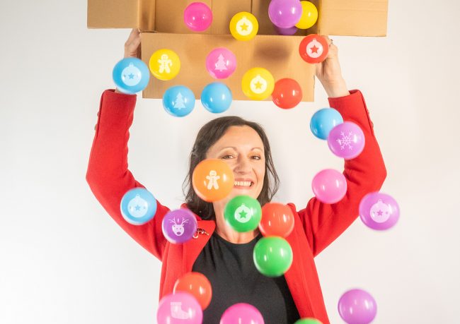 Yvonne Gorman at Derby Essential Print Services Christmas Printing Yvonne is holding a box, tipping out lots of colourful baubles. Yvonne is smiling.